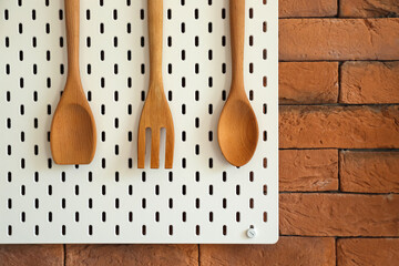 Peg board with wooden spatulas hanging on brick wall