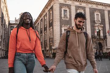 Biracial couple of young people walking in the city center holding hands