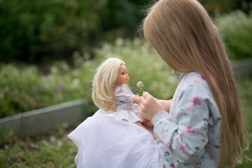 a girl walks in the garden with her favorite doll playing