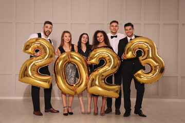 Happy friends with golden 2023 balloons indoors. New Year celebration