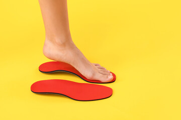 Female foot and red orthopedic insoles on yellow background