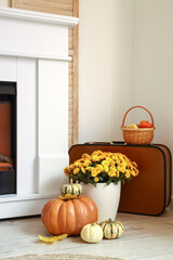 Fototapeta premium Vase with flowers, pumpkins and fallen leaves near fireplace in light room