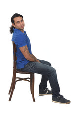 side view of man with ponytail and casual clothing  sitting a chair looking at camera on white background