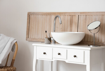 Table with sink, toothbrush and mirror near light wall in bathroom