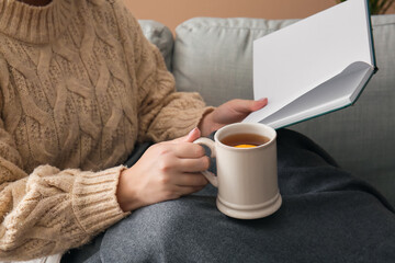 Woman holding cup of tea and opened book, closeup