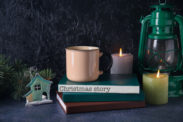 Books with glowing candles, cup and lantern on dark background. Christmas story