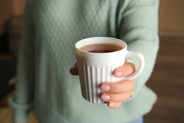 Woman drinking tasty tea indoors, closeup