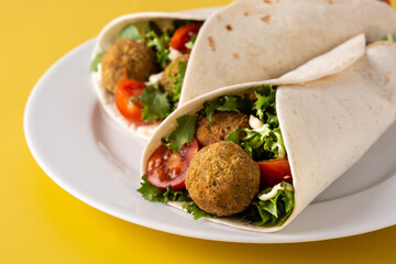 Tortilla wrap with falafel and vegetables on yellow background. Close up