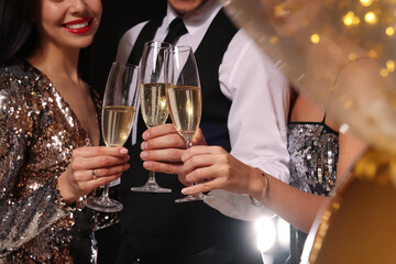 Friends with glasses of sparkling wine celebrating New Year on black background, closeup