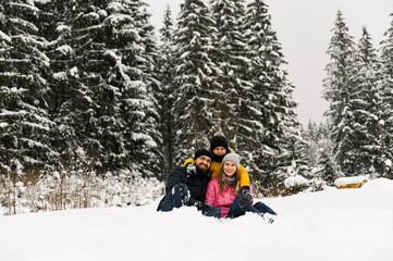 Fototapeta na wymiar Happy family have fun in winter forest and looking at camera. Mother, father and son playing with snow. Family Christmas concept. Enjoying spending time together