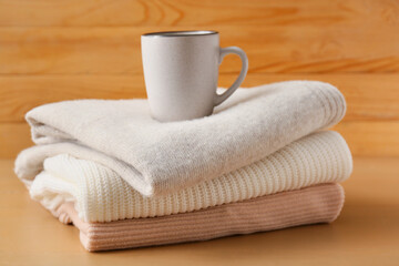 Fototapeta na wymiar Stack of different cozy sweaters and cup of coffee on wooden background