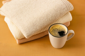 Fototapeta na wymiar Stack of different cozy sweaters and cup of coffee on wooden background