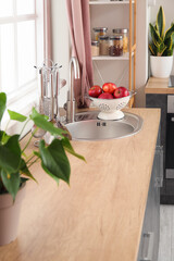 Colander with apples on silver sink in modern kitchen