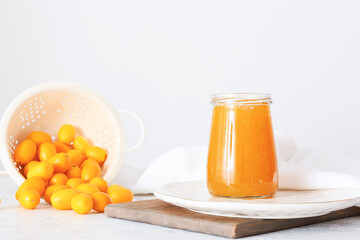 Jar of tasty kumquat jam and fresh fruits on light background