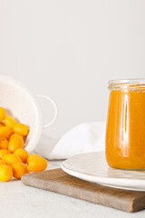 Jar of tasty kumquat jam and fresh fruits on light background, closeup