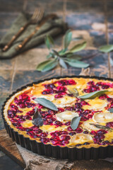 Cranberry goat cheese tart with sage on rustic blue background, vertical