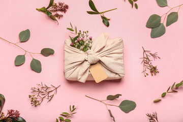 Composition with gift box wrapped in cotton fabric and floral decor on pink background