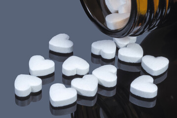 White pills in the form of hearts falling out of a glass bottle