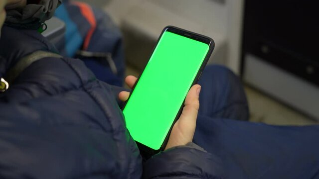 Back view of kid watch smart phone with green screen and browsing online in train. Mock up for watching content on cell phone. Blank digital phone in hand of boy stitting indoors in public transport