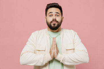Obraz premium Young smiling happy man 20s wear trendy jacket shirt hands folded in prayer gesture, begging about something isolated on plain pastel light pink background studio portrait. People lifestyle concept