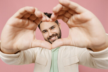 Close up young smiling happy man 20s wearing trendy jacket shirt showing shape heart look through...