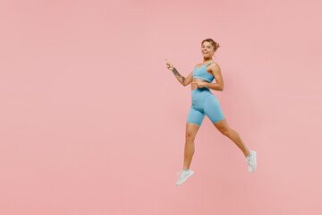 Full size young athletic fitness trainer instructor woman wearing blue tracksuit spend time in home gym jump high point finger aside on area isolated on plain pink background. Workout sport concept