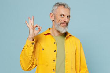 Elderly satisfied caucasian fun gray-haired mustache bearded man 50s wear yellow shirt showing okay ok gesture isolated on plain pastel light blue background studio portrait. People lifestyle concept.
