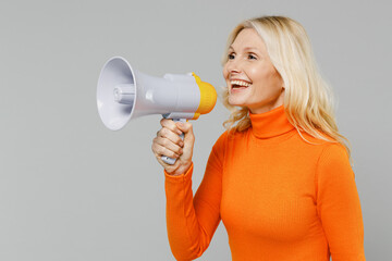 Elderly smiling happy blonde woman 50s in orange turtleneck hold scream in megaphone announces...