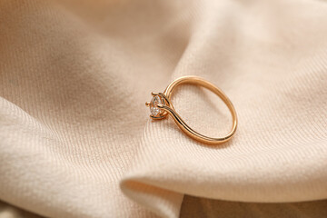 Golden engagement ring on beige fabric background, closeup