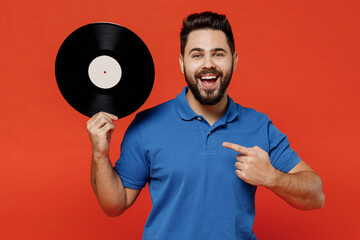 Young excited happy satisfied amazed cool fun man 20s in basic blue t-shirt point finger on hold retro vintage music plate isolated on plain orange background studio portrait People lifestyle concept