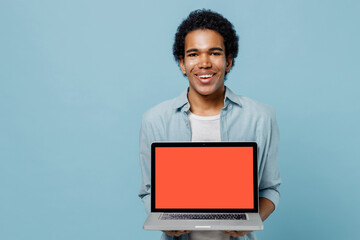 Smiling young black curly man 20s years old wears white shirt hold use show work on laptop pc computer with blank screen workspace area isolated on plain pastel light blue background studio portrait.