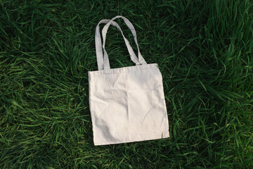 White cotton or mesh eco bag on green grass background. Zero waste, no plastic, eco friendly shopping, recycling concept. Blank mockup shopper with place for artwork or text. Flat lay, copy space