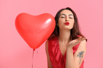 Beautiful young woman with balloon blowing kiss on color background. Valentine's Day celebration