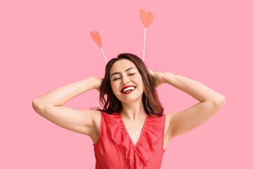 Funny young woman with red hearts on pink background. Valentine's Day celebration