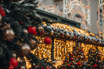 Christmas tree with festive red golden Christmas balls and shiny festive garlands on the street in the winter holiday season. Magic New Year atmosphere and outdoor decoration