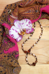 Composition with orchid flower, silk scarf and necklace made of glass beads and pearls for greeting card, magazine cover, etc., vertical orientation, selective focus.