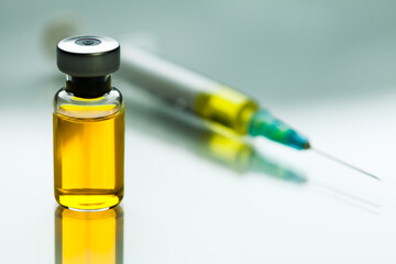 Yellow liquid in glass ampoule vial next to syringe with needle