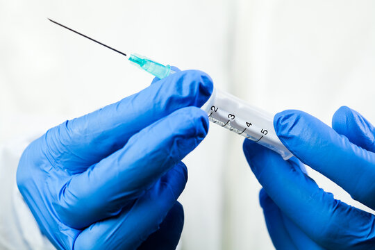 Close up of hands in blue gloves holding syringe with needle