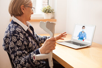 Senior woman at home talking to young female doctor over laptop video call