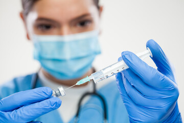 Female doctor holding syringe with needle and glass vaccine ampoule
