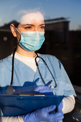Portrait of young female doctor looking through hospital window