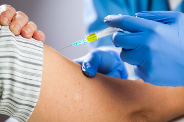 Closeup of hand in blue protective gloves injecting vaccine dose shot into patients arm
