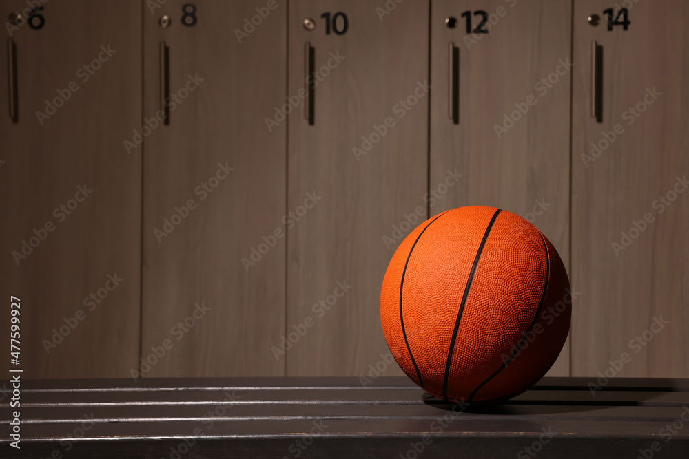 Wall mural Orange basketball ball on wooden bench in locker room. Space for text