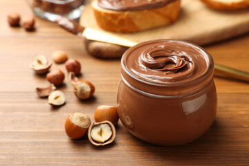 Glass jar with tasty chocolate hazelnut spread and nuts on wooden table. Space for text