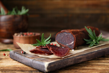 Delicious dry-cured beef basturma with rosemary and peppercorns on wooden table, closeup