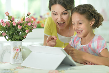 happy mother and daughter using tablet together at home