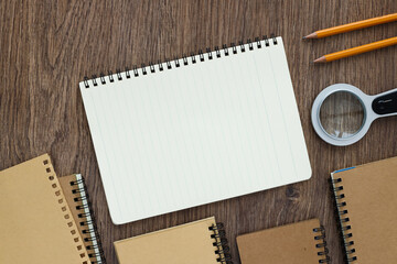 Open notebooknear a magnifying glass and pencils on wooden desk