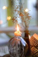 Two candle holders with lit candles, vase with gypsophila flowers and soft knitted blanket. Bokeh lights in the background. Hygge at home. Selective focus.