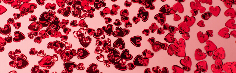 top view of shiny red confetti hearts on pink, banner.