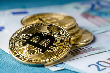 Physical Gold Bitcoin Coin against euro bills.